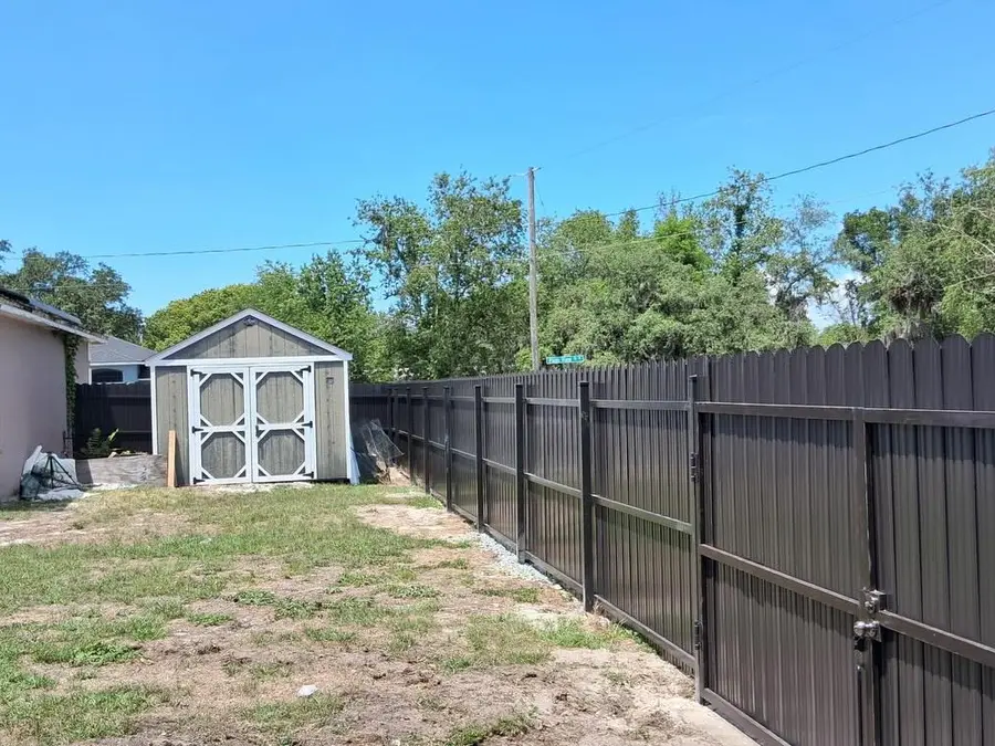 Fence company Kissimmee, FL — dark privacy fence with gate opening to a spacious backyard